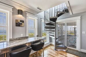 Eine moderne Küche mit Marmorarbeitsplatte, schwarzen Barhocker und einer Wendeltreppe, die zu einem Balkon mit Meerblick führt.