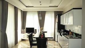 Una sala de estar moderna con una mesa de comedor, sillas negras, un televisor y una cocina con armarios y encimera.