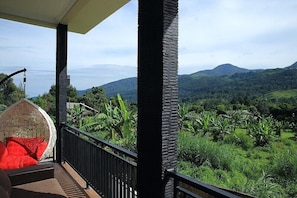 A balcony with a wicker chair and a view of lush green hills. - Avilla Resort Puncak (Cisarua)