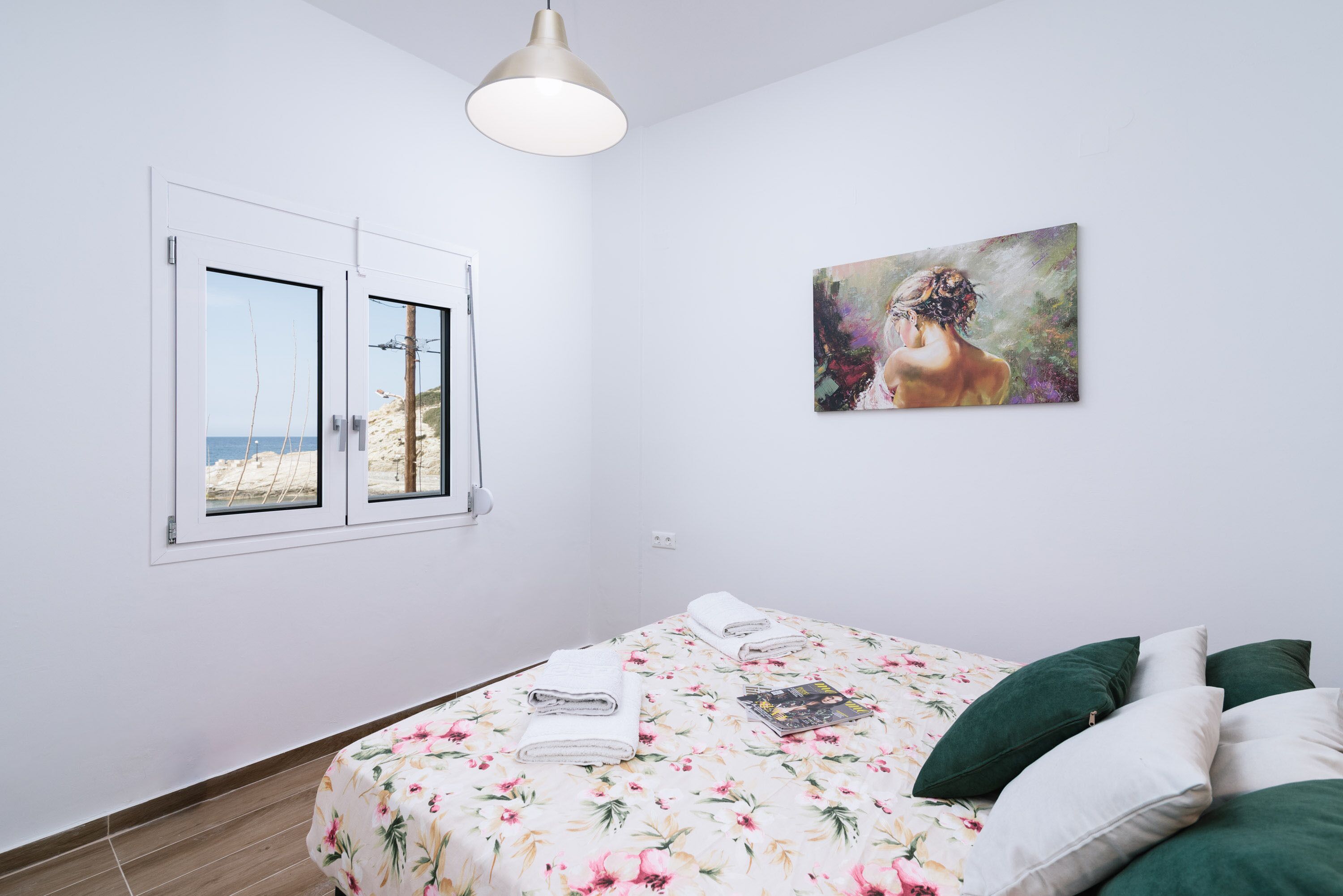 Une chambre avec un lit, une fenêtre donnant sur la plage et un tableau accroché au mur.