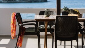 A dining area with a table and chairs, a hanging light fixture, and a view of the sea and a rocky outcrop. - Beach front apartment with swimming pool ideal for families (Ligaria Beach)