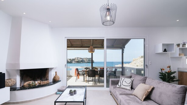 A modern living room with a fireplace, a sofa, a coffee table, and a view of the sea through large sliding doors. - Beach front apartment with swimming pool ideal for families (Ligaria Beach)