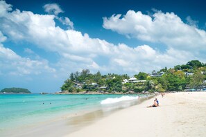A beach with clear turquoise water, a sandy shore, and buildings on a hillside in the background. - Grand Kata VIP - Kata Beach (Karon)
