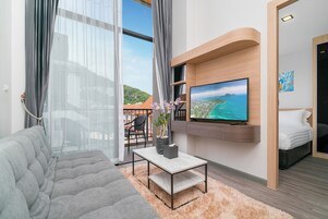 Una sala moderna con un sofá, una mesa de centro, un televisor montado en la pared y vistas de la ciudad a través de amplias ventanas.