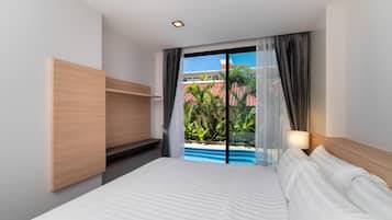 Habitación de hotel con cama, estante de madera, ventana con cortinas y vista a una piscina y palmeras.