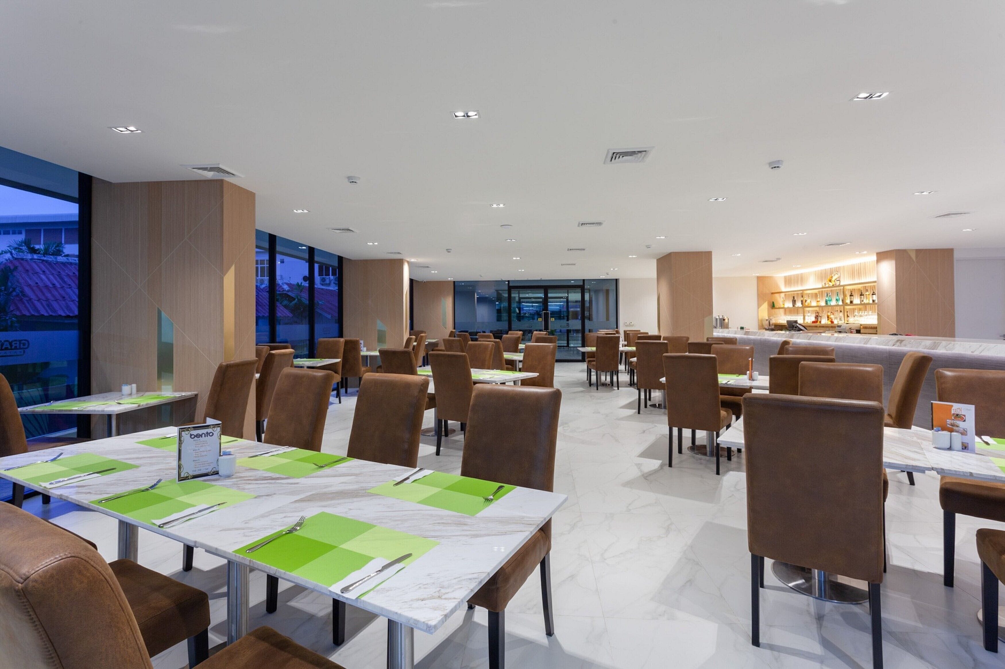 A modern dining area with marble tables, brown leather chairs, and a bar in the background.