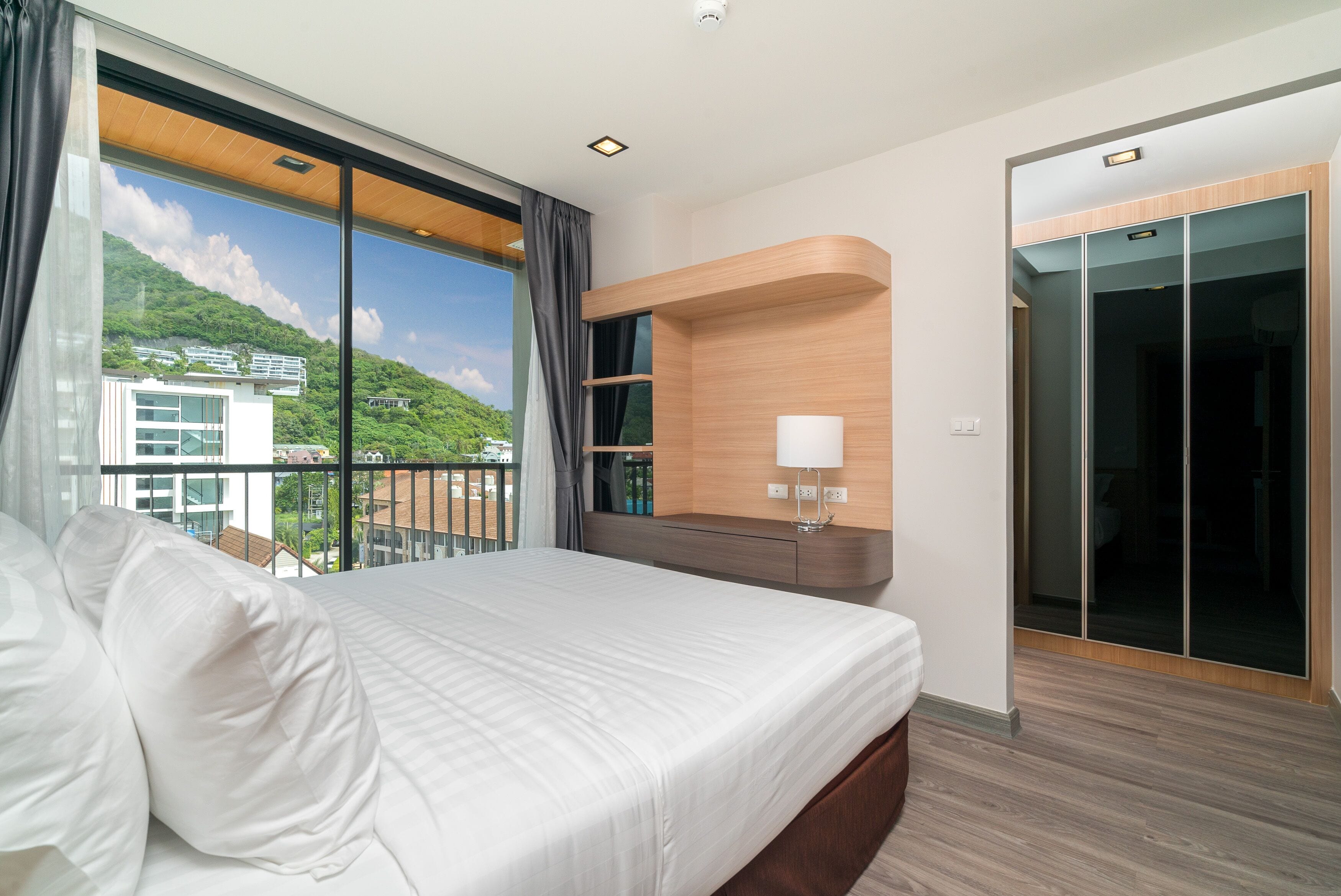 Une chambre d’hôtel moderne avec un grand lit, une étagère intégrée avec une lampe et un placard à portes coulissantes en verre.