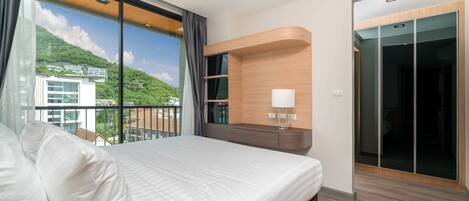 A modern hotel room with a large bed, a built-in shelf with a lamp, and a sliding glass door closet.