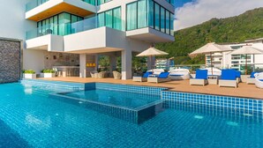 Un hotel moderno con piscina, sillas de descanso y una zona de bar.