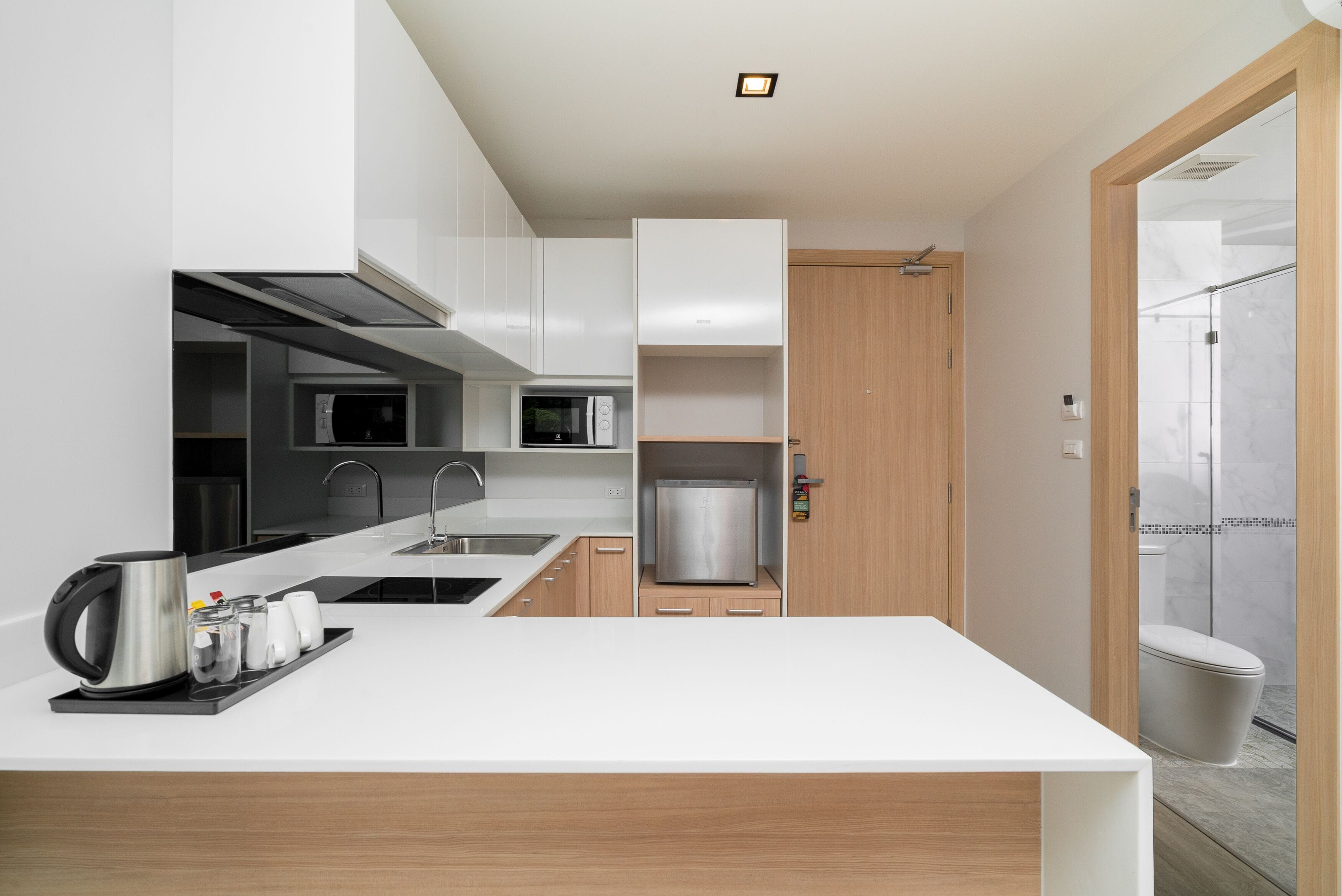 A modern kitchen with white cabinetry, a stainless steel refrigerator, and a coffee station.