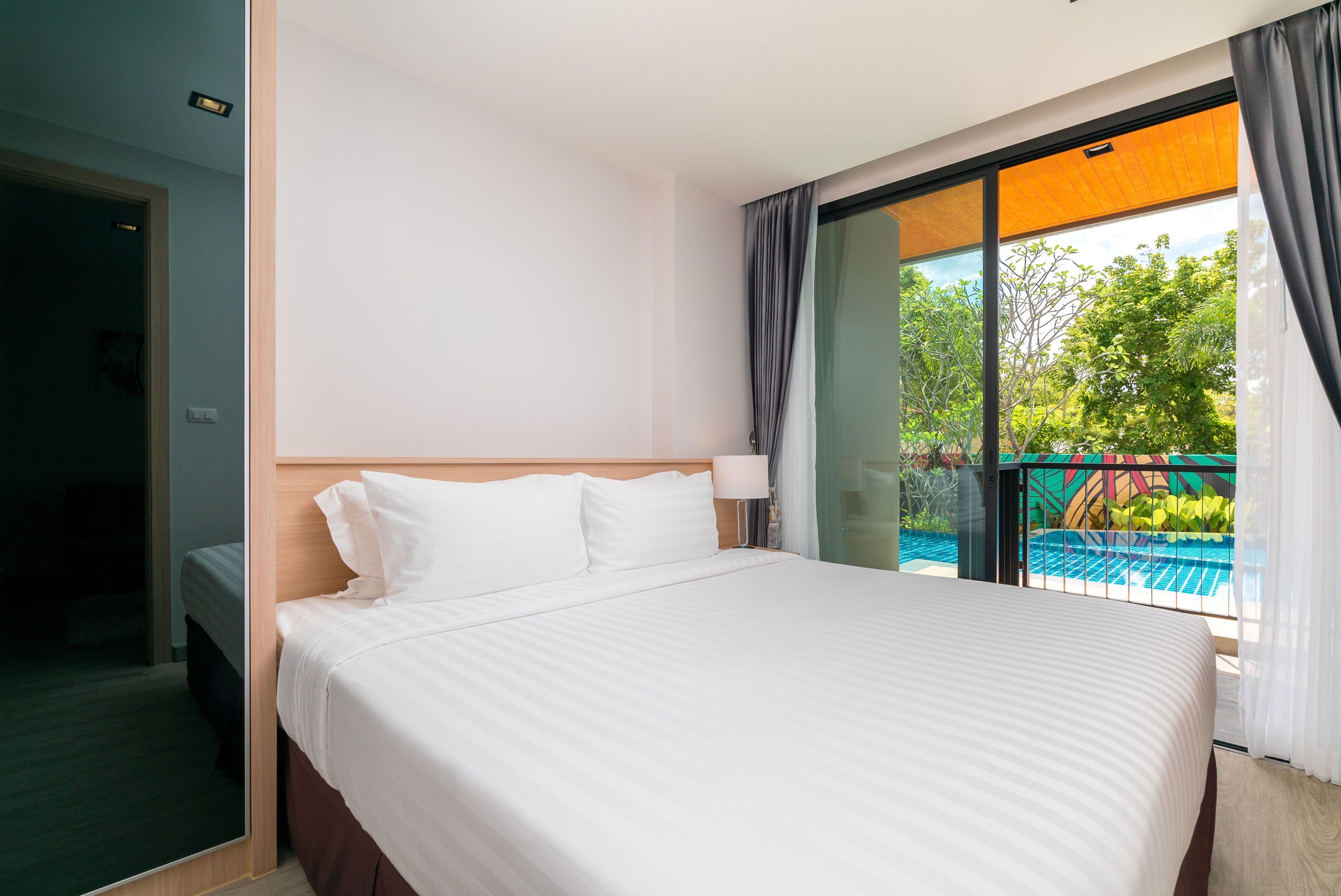 A hotel room with a large bed, a view of a swimming pool, and a sliding glass door to the outdoors.