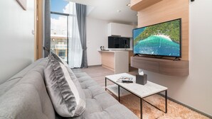 Un moderno salón con un sofá gris, un televisor de pantalla plana montado en la pared, una mesita de centro y vistas al balcón.