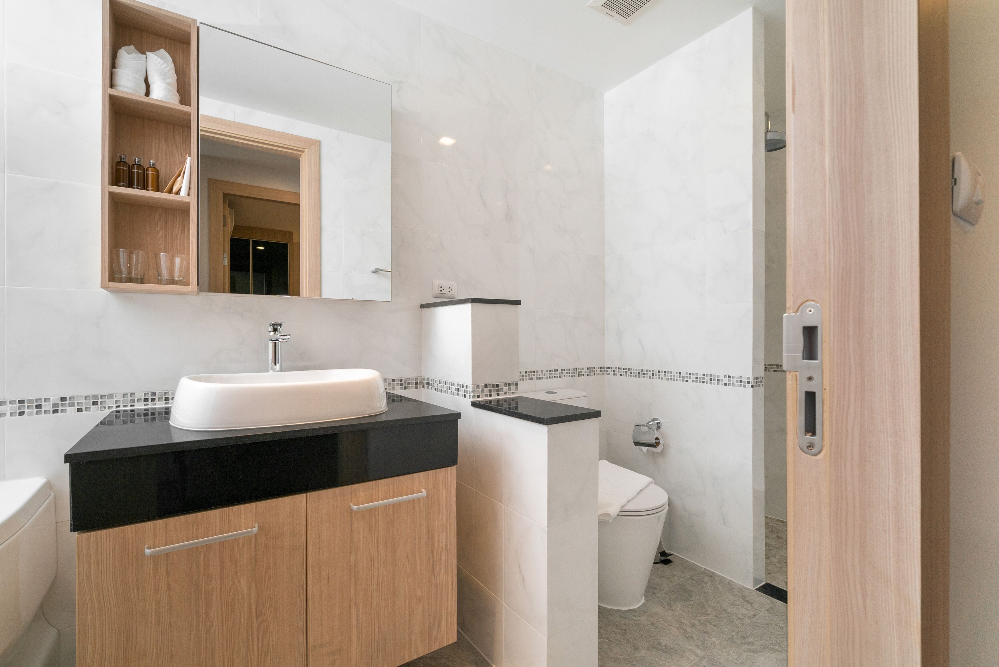 A modern bathroom with a black countertop sink, wooden cabinets, a white toilet, and a mirror above the sink.