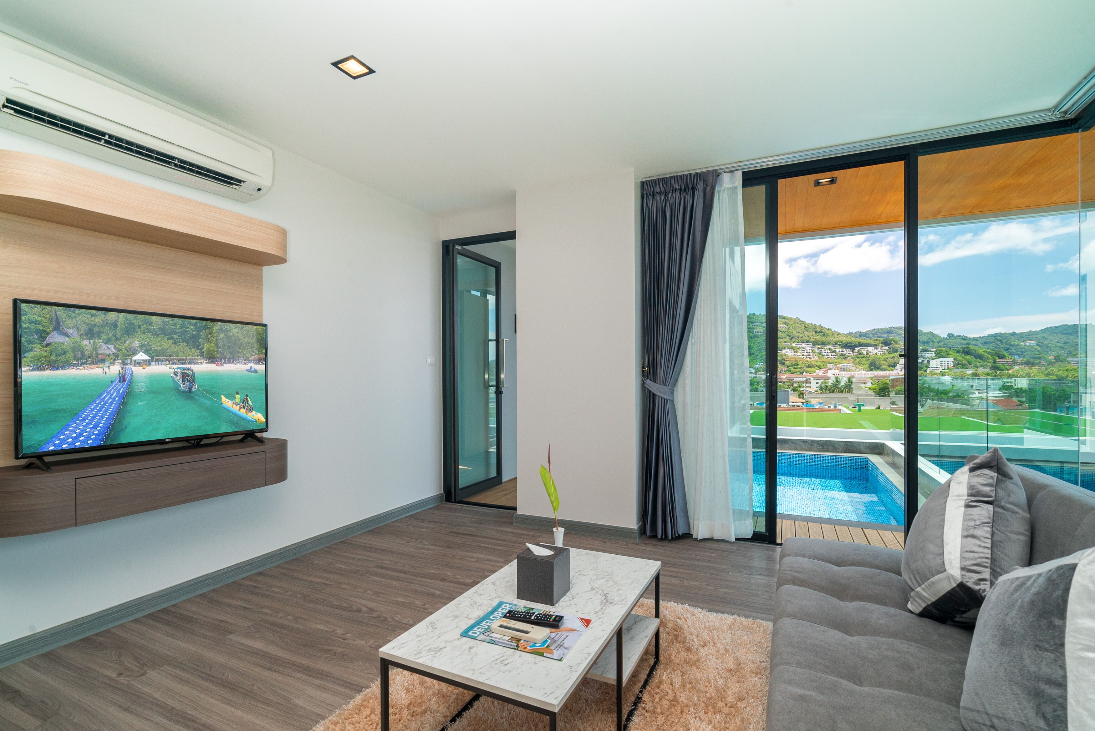 Ein modernes Wohnzimmer mit einem Flachbildfernseher, einem Marmortisch, einer Couch und Blick auf einen Swimmingpool und Hügel.