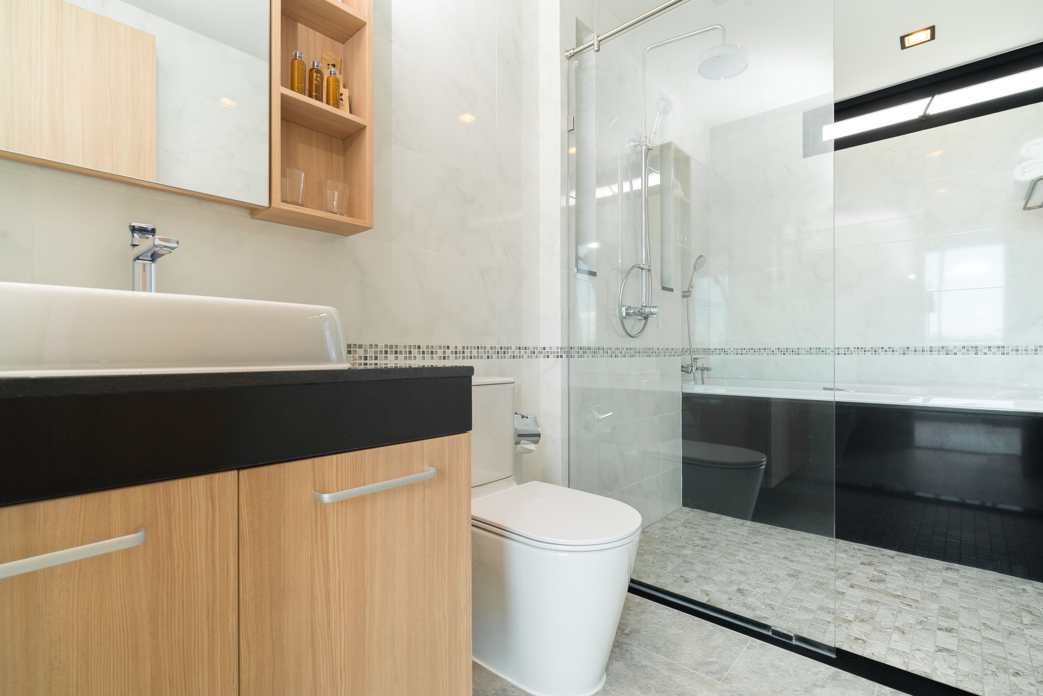 Un baño moderno con ducha de vidrio, inodoro blanco y tocador de madera con encimera negra.