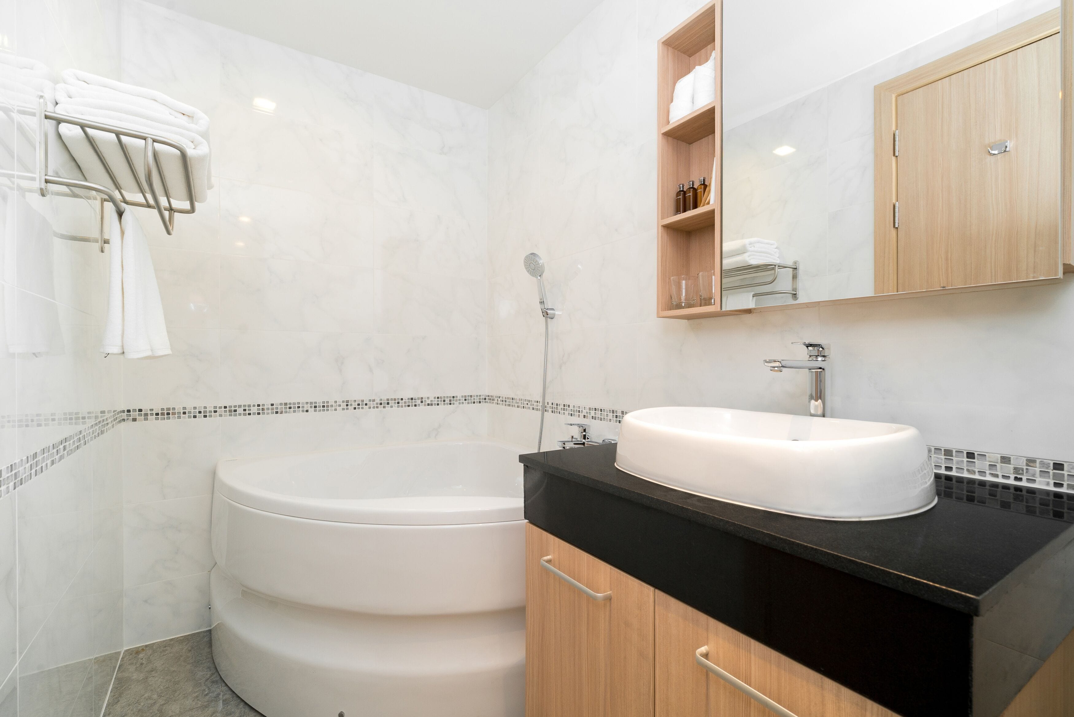 Un bagno moderno con una vasca freestanding, un lavabo con piano nero e un mobile contenitore in legno.