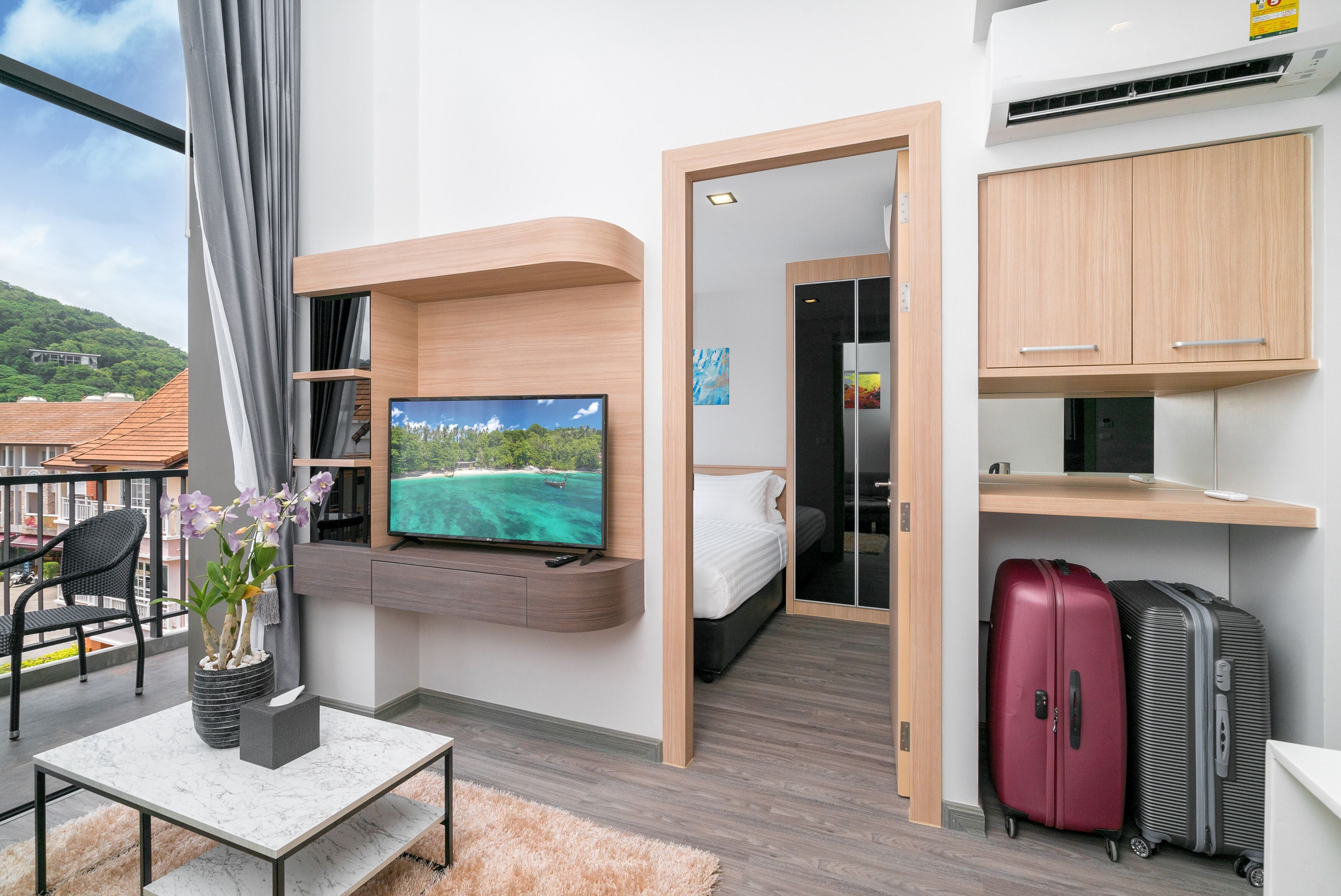 A modern hotel room with a TV, a bed, a desk, and a suitcase.