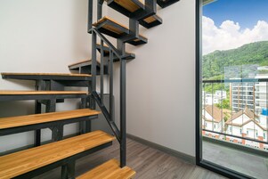 A modern staircase with wooden steps and black metal railings, leading to a balcony with a city view.