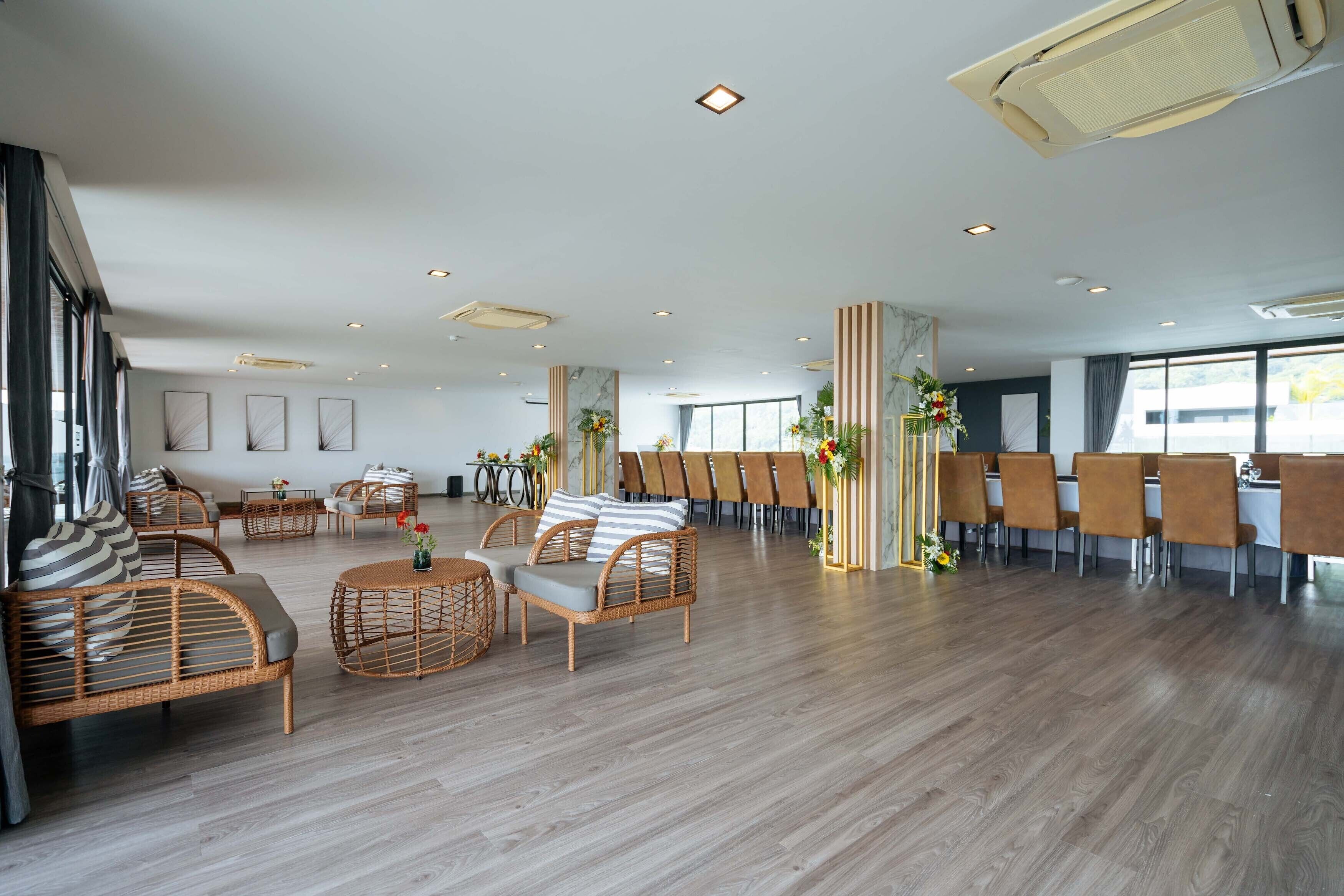 A spacious hotel lobby with wicker furniture, a long dining table, and large windows.