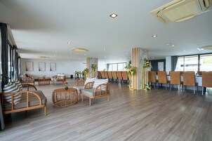 Un amplio hall de hotel con mobiliario de mimbre, una larga mesa de comedor y ventanas grandes.