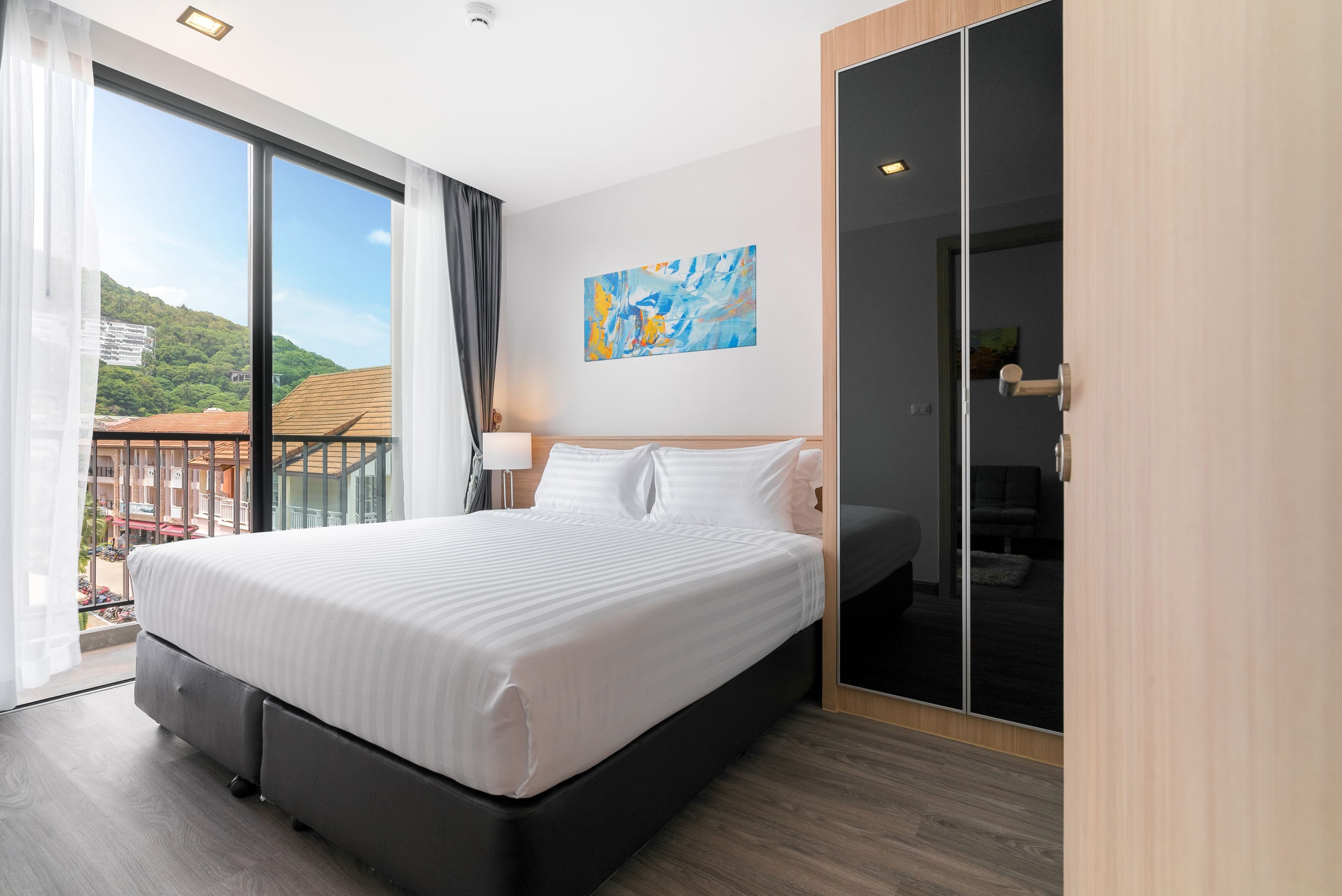 Una camera d'albergo moderna con un letto grande, un balcone con vista sul verde, un quadro appeso al muro e un armadio con ante scorrevoli.