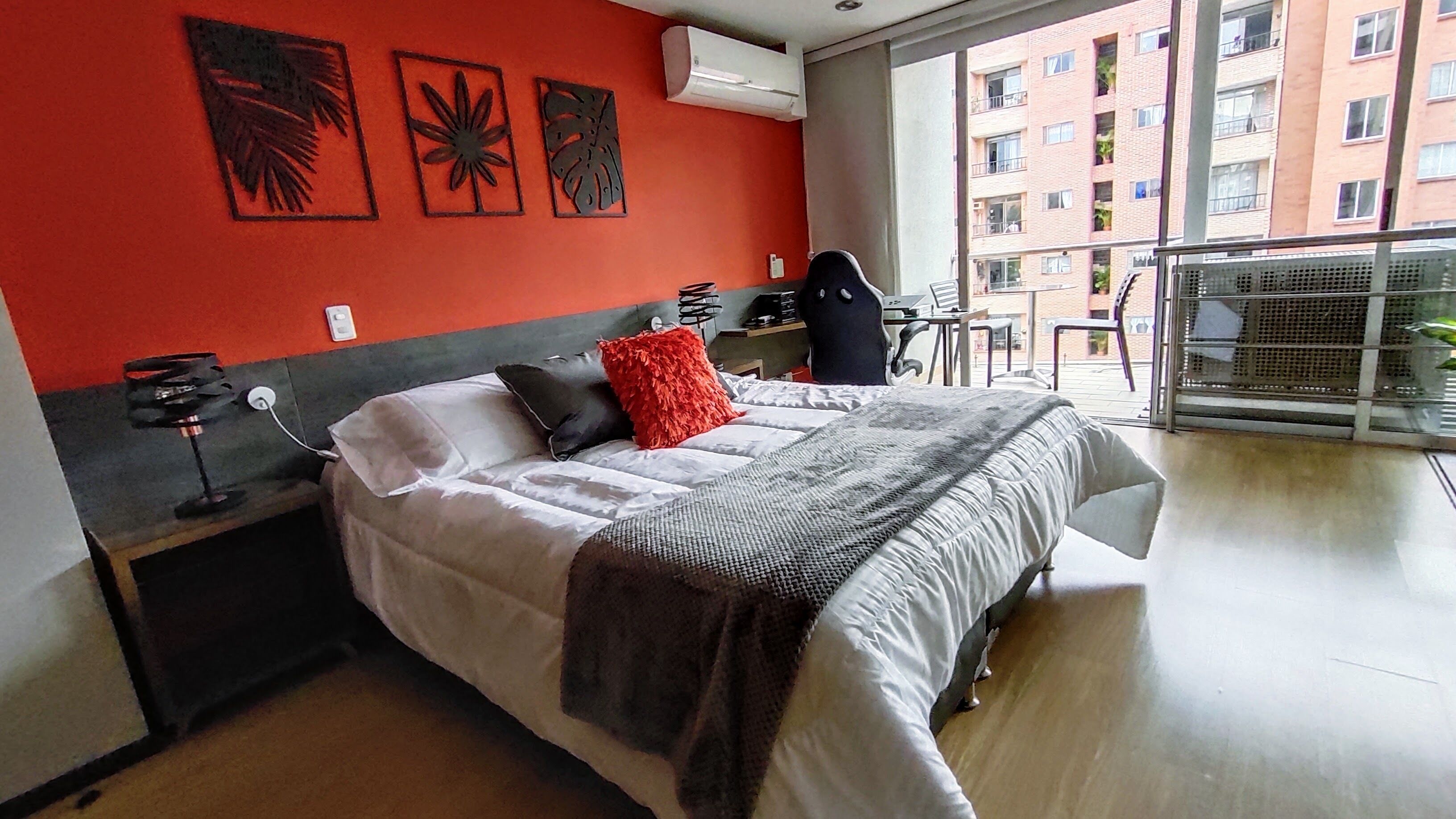 A hotel room with a bed, a desk, and a chair. There is a window with a view of buildings outside.