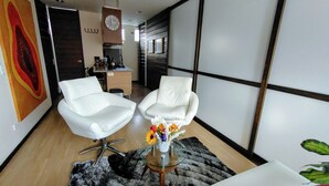 Un salon moderne avec deux fauteuils en cuir blanc, une table basse en verre agrémentée d’un arrangement floral, et un grand tableau abstrait accroché au mur.