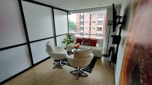 Un salon moderne comprenant un canapé, deux fauteuils, une table basse et une vue sur un immeuble en briques rouges, visible à travers de grandes fenêtres.