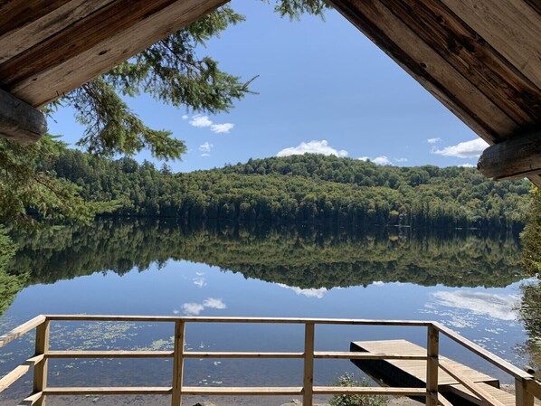 A wooden cabin with a view of a calm lake and forested hills.