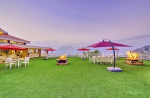 An outdoor patio with artificial grass, white furniture, and red umbrellas.