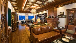 A spacious living room with a leather sofa, wooden bookshelves, and a chandelier. - MAYFAIR Himalayan Spa Resort (Kalimpong)