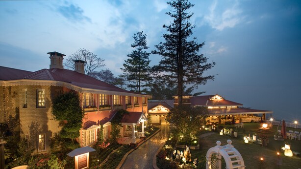 A large, well-lit hotel with a central courtyard, multiple buildings, and a variety of outdoor seating areas. - MAYFAIR Himalayan Spa Resort (Kalimpong)