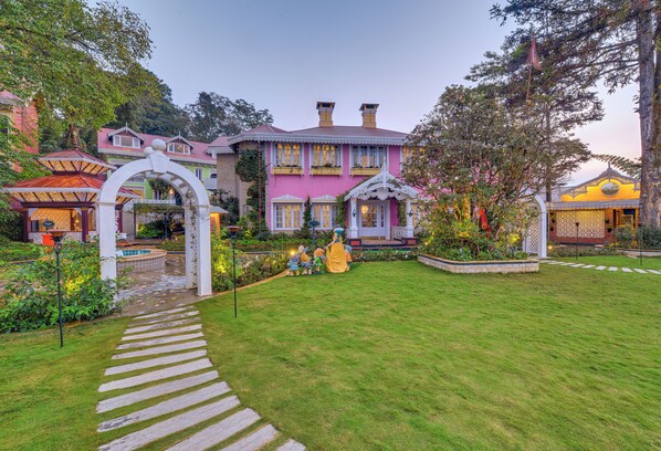 A large, colorful house with a well-maintained garden and a pathway leading to the entrance.