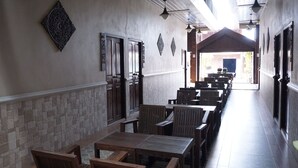 Um corredor comprido com mesas e cadeiras de madeira, paredes de pedra e luminárias pendentes.