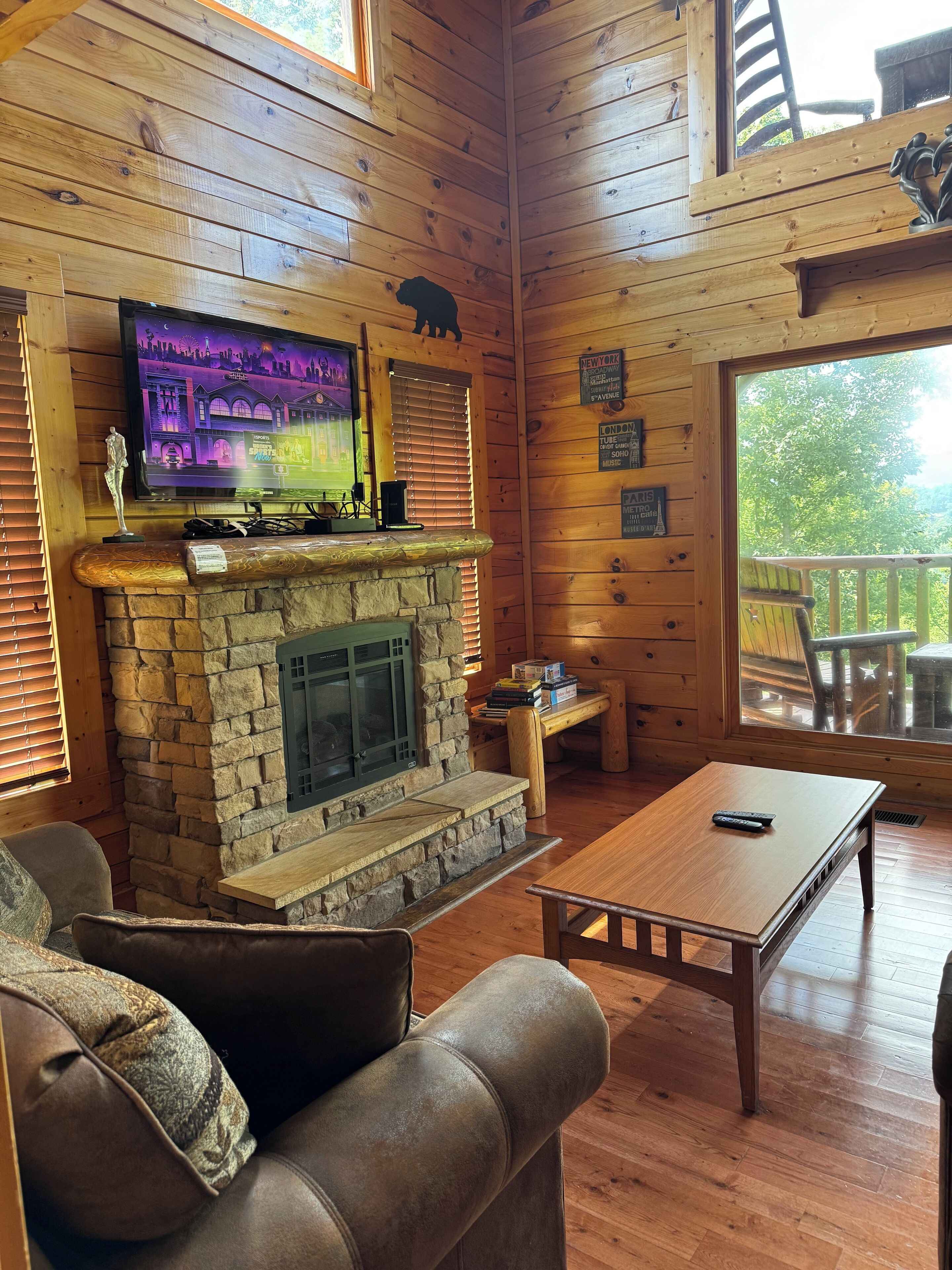 A cozy cabin interior with a stone fireplace, wooden walls, a television mounted above it, and a wooden table.