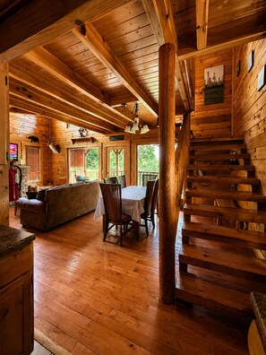 A wooden cabin interior with a dining area, sofa, and staircase.