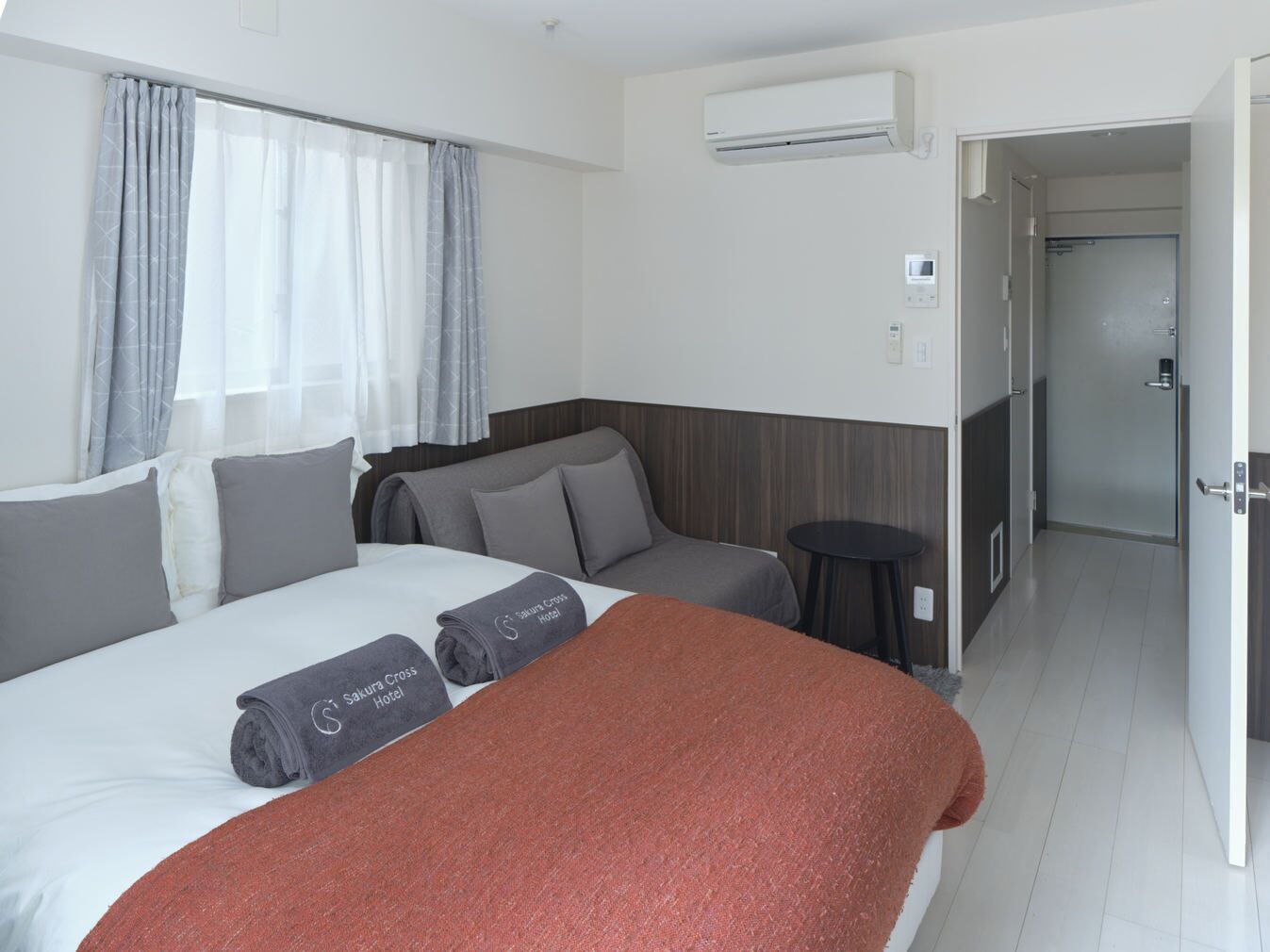 Camera d'albergo con un letto, un divano, un tavolino, un condizionatore d'aria e una porta che dà su un bagno.