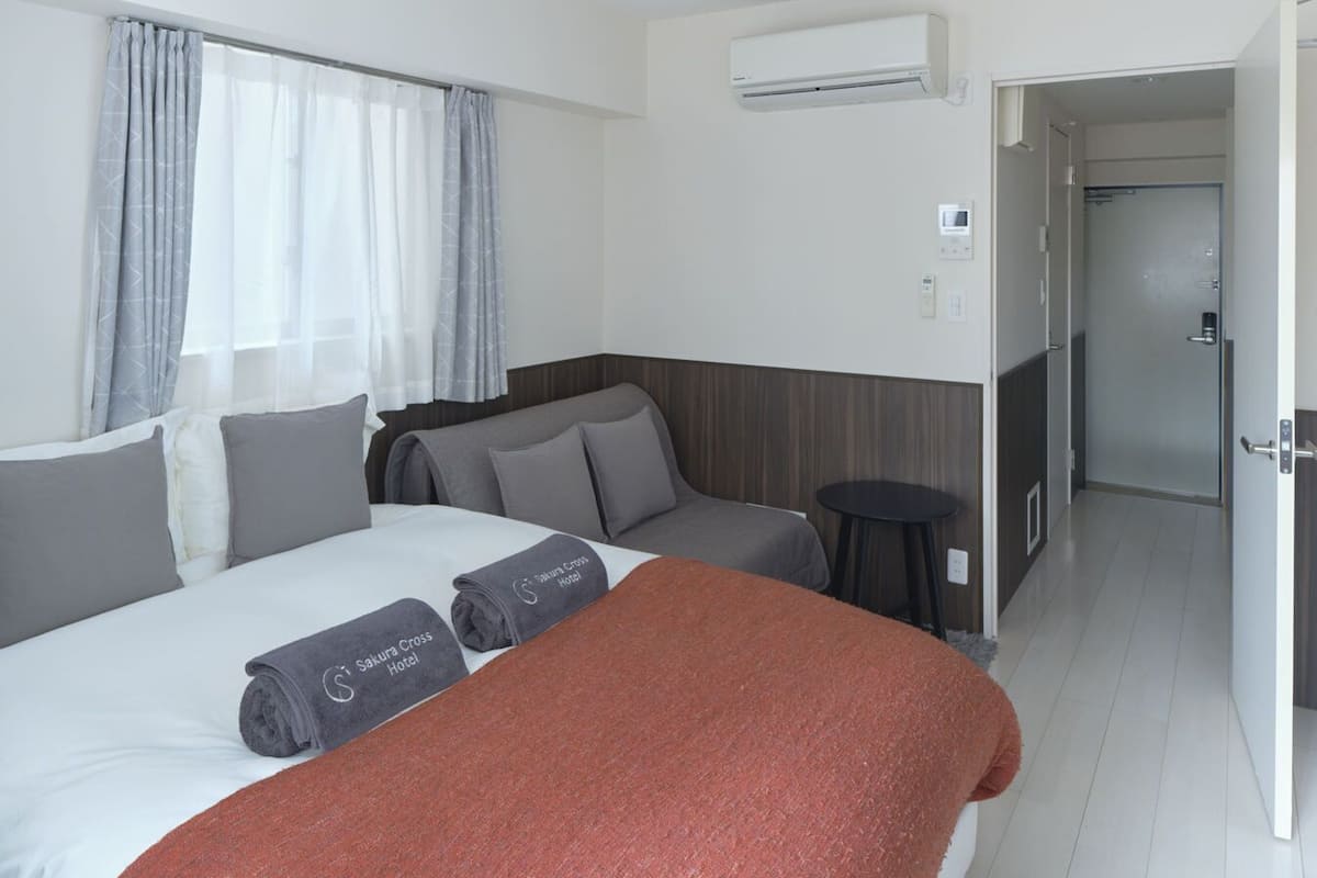 Habitación de hotel con cama, sofá, una mesita, equipo de aire acondicionado y puerta que da a un baño.