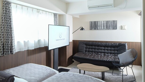 A hotel room with two beds, a sofa, a small table, and a TV.