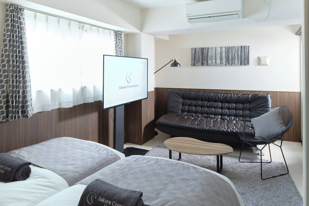 Ein Hotelzimmer mit zwei Betten, einem Schlafsofa, einem kleinen Tisch und einem Fernseher.