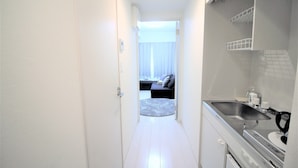 A narrow hallway leading to a bedroom with a bed, a bathroom with a sink, and a kitchenette with a stove.