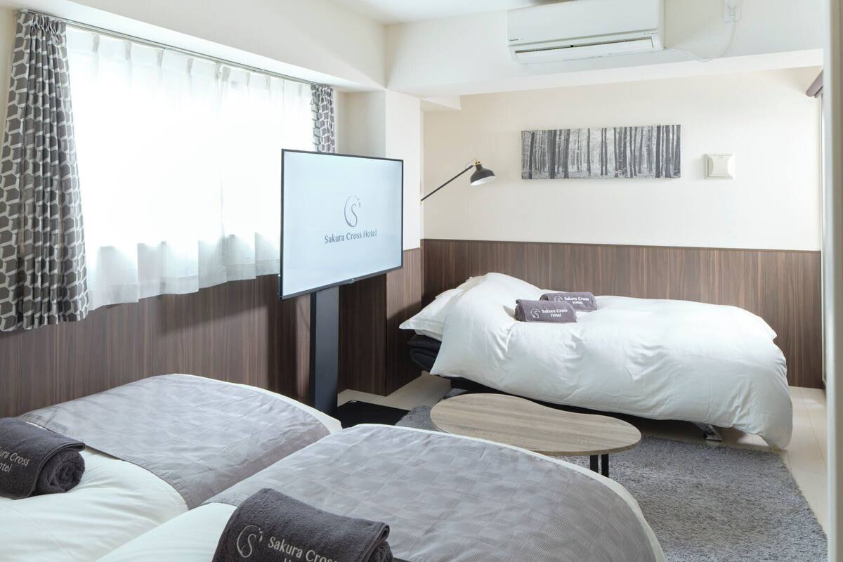 Ein Hotelzimmer mit zwei Betten, einem Fernseher, einem Schreibtisch und einem an der Wand hängenden Kunstwerk.