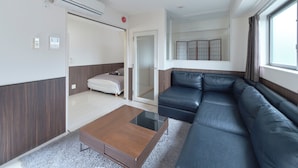 A modern hotel room with a sofa, a small table, a bed, and a sliding door leading to a balcony.