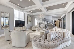 A spacious living room with a large sectional sofa, a television, and a chandelier. - The Atlantis at Reunion | Luxe Mansion w/ Private Pool, Arcades, and Themed Rooms Near Disney (Four Corners)