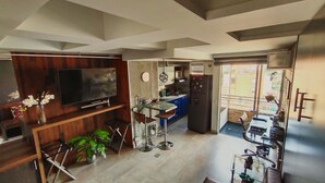 A compact living space with a TV, kitchen area, and a balcony.