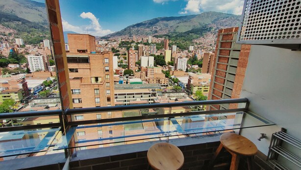 A balcony with a view of a cityscape, including buildings and mountains.