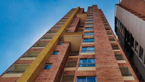 A tall building with multiple floors, featuring a central yellow structural element and numerous windows.
