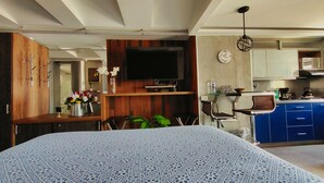 A modern kitchen with blue cabinets, a dining area with a patterned tablecloth, and a TV mounted on the wall.