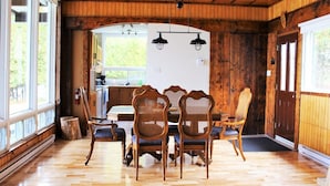 A wooden interior with a dining table and chairs, a kitchen area, and large windows. - Lakefront Chalet Mont Tremblant - Spectacular view - WIFI (CITQ 294661) (Lac-Supérieur)
