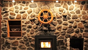 A stone fireplace with a wooden wheel, a shelf with a bird, and a lit fire. - Lakefront Chalet Mont Tremblant - Spectacular view - WIFI (CITQ 294661) (Lac-Supérieur)